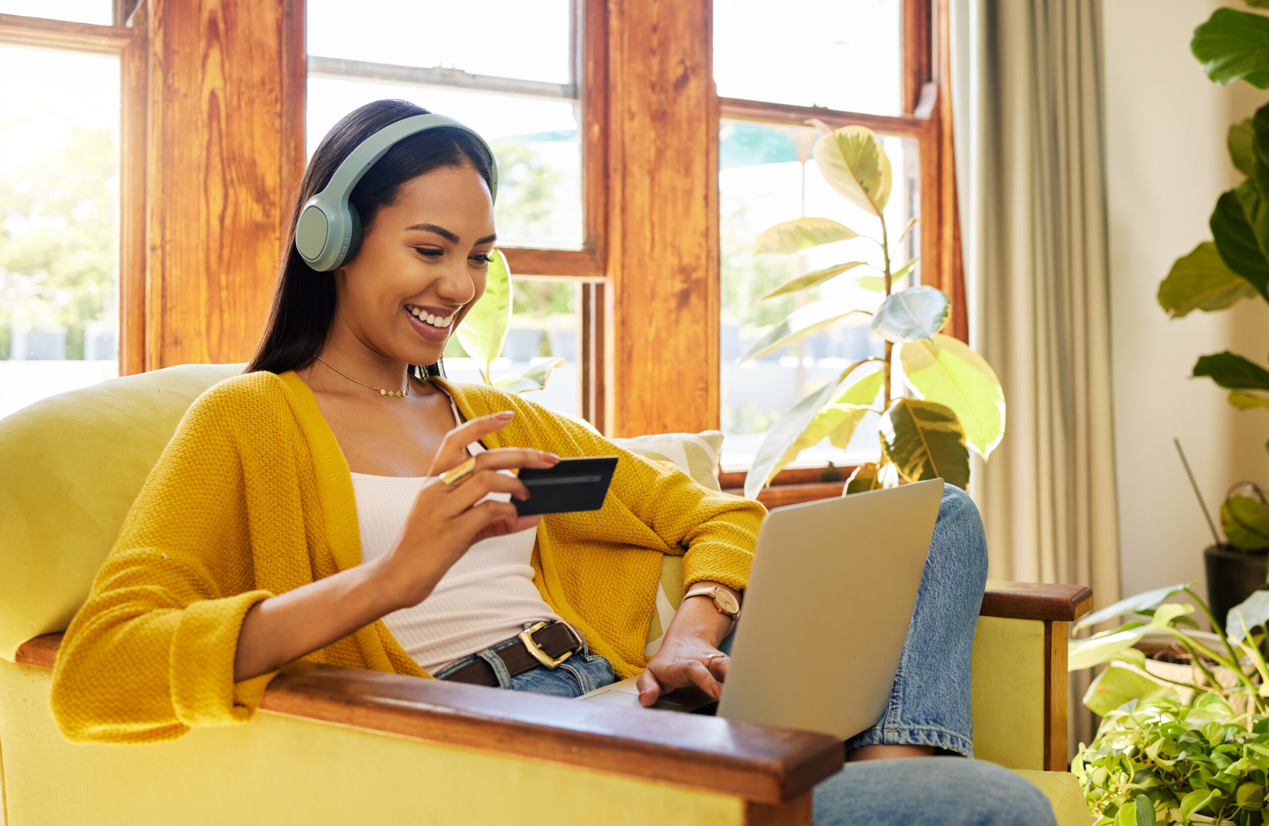 Happy woman, laptop and credit card with ecommerce and headphones to listen to music while online shopping. Female relax at home, radio streaming with fintech, internet banking and payment success